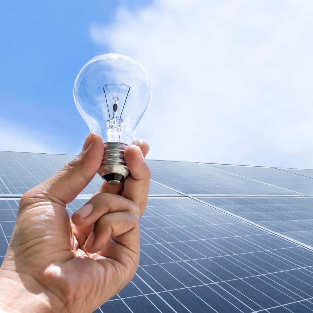 Hand holding lightbulb with solar panels in the background